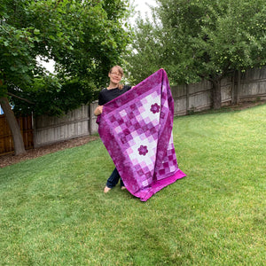 What has been under my needle lately? Picture of me in my yard, holding a purple version of the Irish Woodland quilt