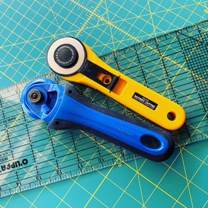 Two rotary cutters and a ruler on a green mat