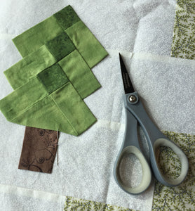 Appliquing trees on the Irish Woodland Quilt green pine tree on a white background with scissors and needle