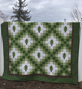 Irish Woodland Quilt in Green Brown and White with tiny trees on a Irish chain. Hanging on a white vinyl fence