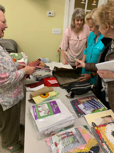 Stash and Sweet Swap at the Quilt Guild Meeting - Ladies standing around a table covered in fabric and patterns