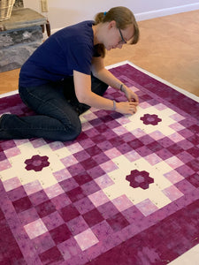 Layering and Pin Basting a Quilt while sitting on the floor. The quilt is violet purple and white